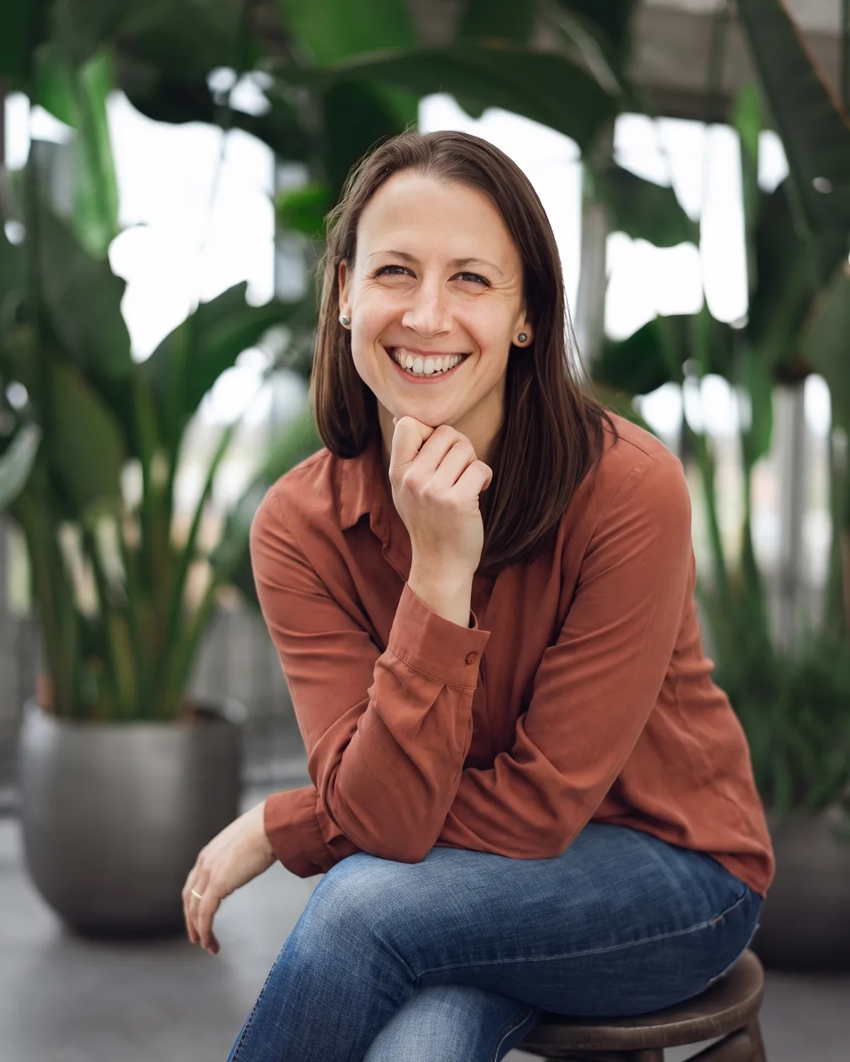Carina Scheffler sitzt lächelnd auf einem Hocker vor großen grünen Pflanzen